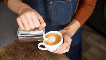 Barista giesst Milchschaum für Latte Art in eine Kaffeetasse - Coffee Coaching Club