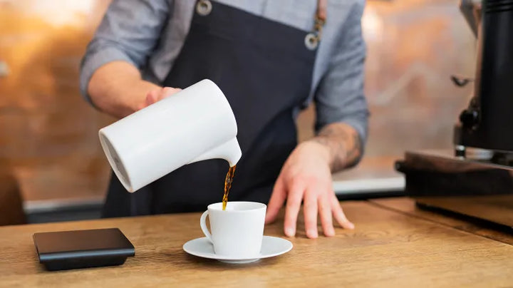Barista giesst frisch gebrühten Kaffee in eine Tasse - Coffee Coaching Club